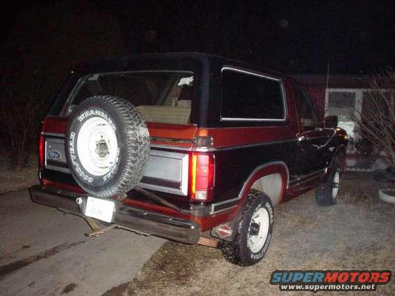 Rear view of a red and black Ford Bronco with a spare tire mounted on the back. The vehicle has a chrome bumper and a license plate