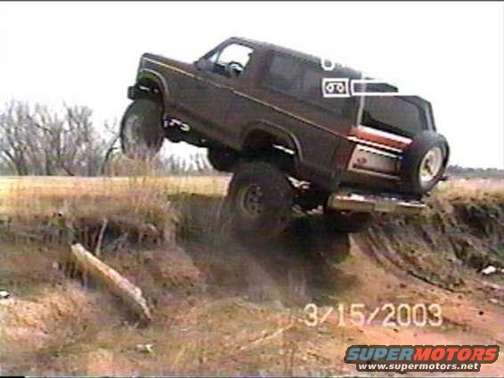 1980s Ford Bronco climbing steep dirt embankment, front wheels off the ground