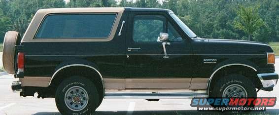 Side view of a black and tan 1988 Ford Bronco with a spare tire mounted on the rear