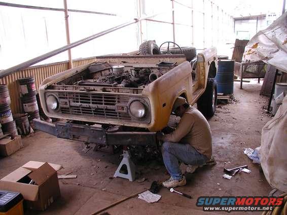 Yellow Ford Bronco with hood open, being worked on by a man
