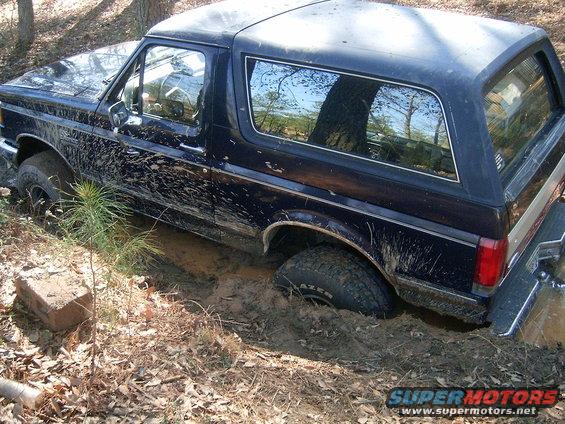 Dark blue SUV stuck in mud and dirt, trees and leaves around