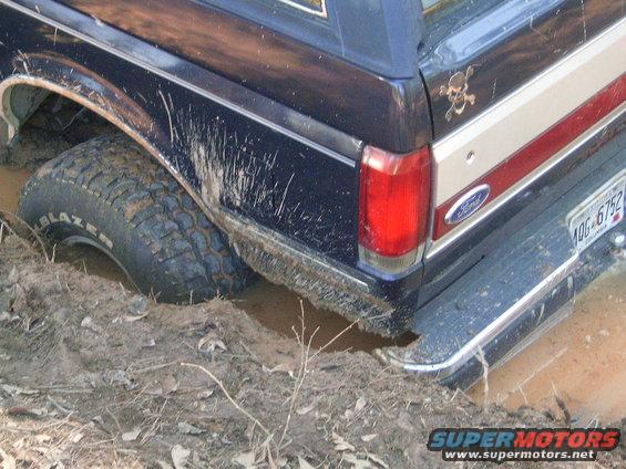 Rear quarter of dark blue Ford Bronco stuck in mud, showing tire, taillight, and license plate 10G-6752