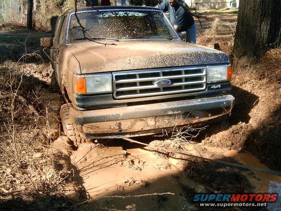 Front view of a muddy 1988 Ford Bronco stuck in mud with 4x4 badge visible