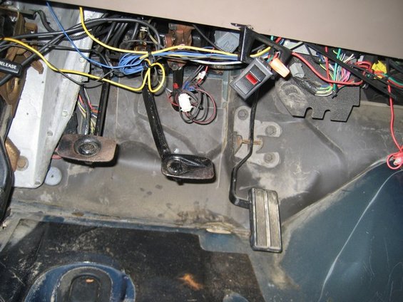 Vehicle interior showing brake, clutch, and accelerator pedals with a lot of exposed wiring and a red switch