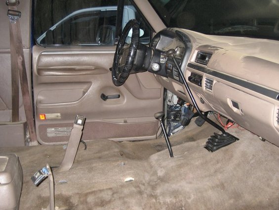 Interior of a truck, showing dashboard, steering wheel, and floor. Another vehicle is visible through the window