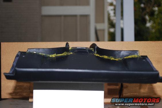 Black plastic car trim piece with yellow adhesive applied
