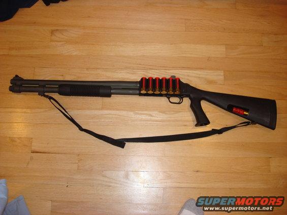 Shotgun with a shell carrier holding six rounds, lying on a wooden floor
