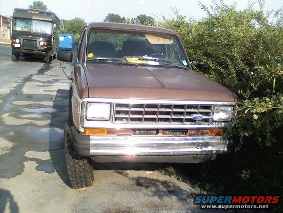 Brown Ford Ranger pickup truck, front view, parked on asphalt next to bushes