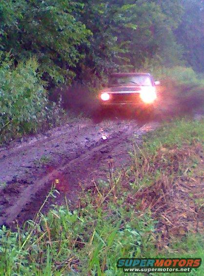 Dark SUV driving through muddy terrain, headlights on