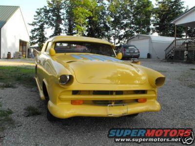 Yellow custom coupe with blue stripes on hood, parked outside