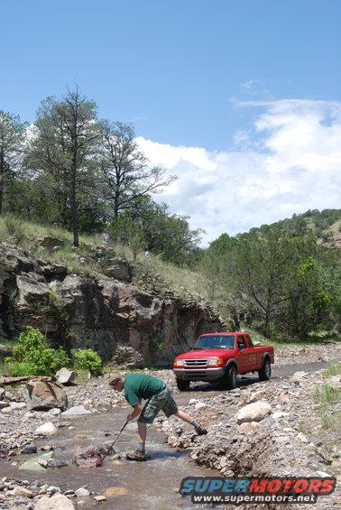 Red pickup truck on a rocky dirt road near a stream