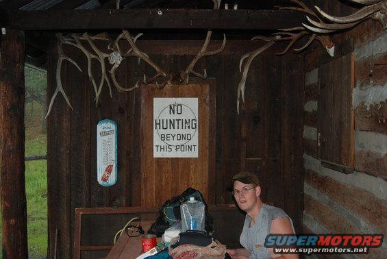 Interior of a rustic cabin with mounted deer antlers and a 'No Hunting' sign