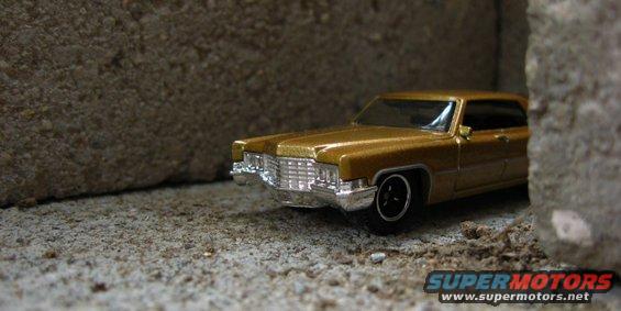 Gold toy car with chrome grille between concrete blocks. Supermotors logo visible