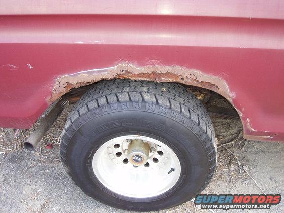 Rear wheel well with rust on a red vehicle. Steel radial tire