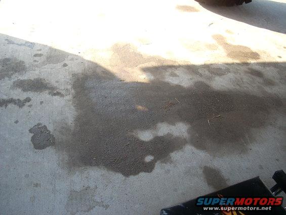 Oil stains on concrete floor with shadows and a partial view of a black object with 'SUPERMOTORS' text