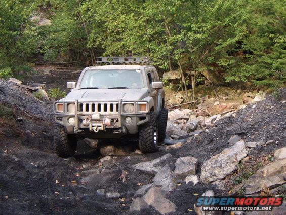 Hummer H3 driving on rocky terrain with trees in background