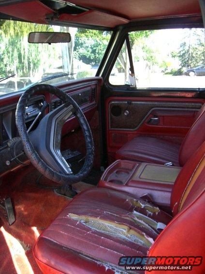 Interior shot of a red vehicle, showing ripped seats, a steering wheel, and dashboard