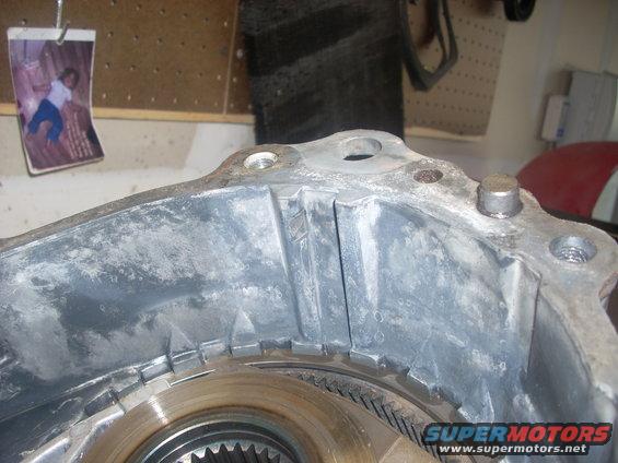 Close-up of a transfer case housing with internal gears visible. A small photo is clipped to a pegboard in the background