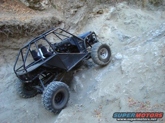 Black off-road buggy with roll cage climbing a steep dirt hill