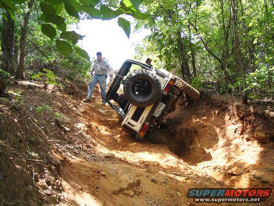 White off-road vehicle tilted on its side in a ditch with a person pulling a rope
