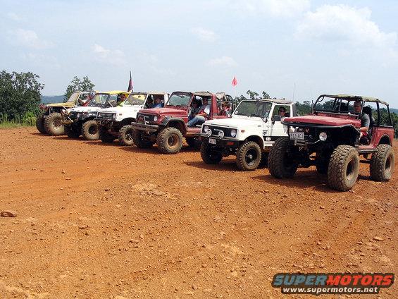 Several modified 1987 Suzuki Samurai vehicles parked in a line on a dirt track