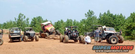 Off-road vehicles on dirt terrain with trees in background