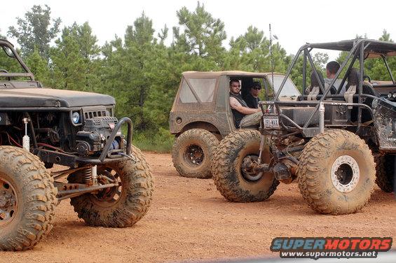 Three modified off-road vehicles with large tires on a dirt track