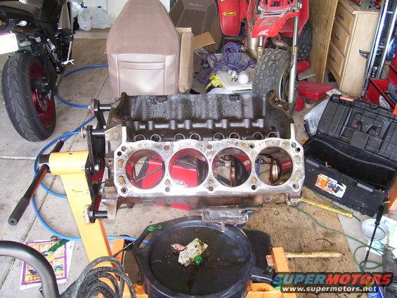 Engine block on an orange stand, with a motorcycle and ATV in the background