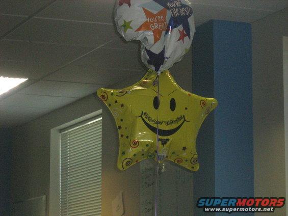 Yellow star balloon with a smiley face and mustache, and a white balloon with stars and text