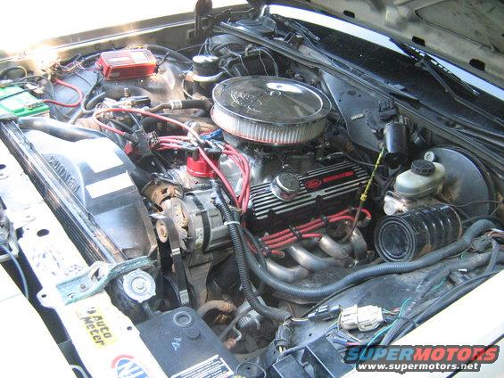 Engine bay showing a V8 engine with aftermarket headers and air cleaner. A red ignition box is visible