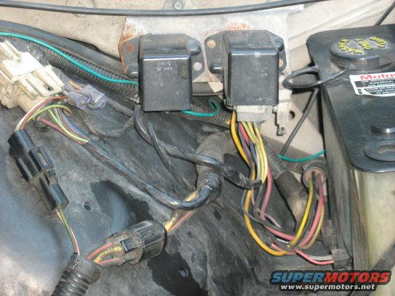 Engine compartment wiring with two black relays and a black plastic fluid reservoir with a yellow cap