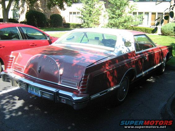 Red Lincoln Continental Mark V with a white vinyl roof and a continental kit on the trunk