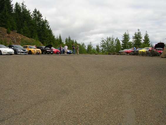 Cars parked on a gravel lot with trees and a cloudy sky