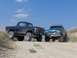 1987 Ford Bronco - A blue 1987 Ford F-Series truck is parked next to a dark-colored older model truck on a dirt road under a blue sky.