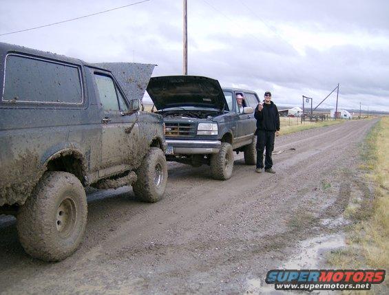 Two muddy 1990 Ford Broncos parked on a dirt road, hoods up