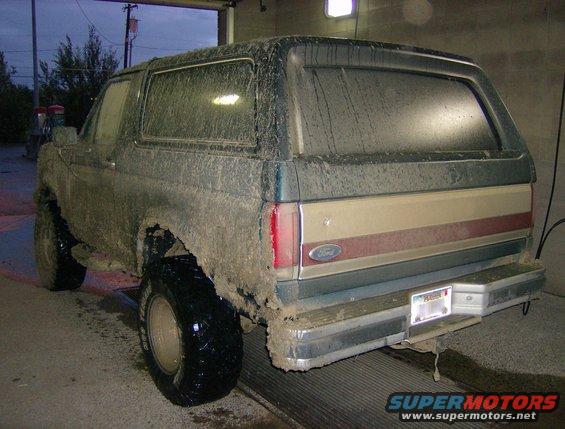1990 Ford Bronco covered in mud, rear 3/4 view, tan and red stripe on tailgate