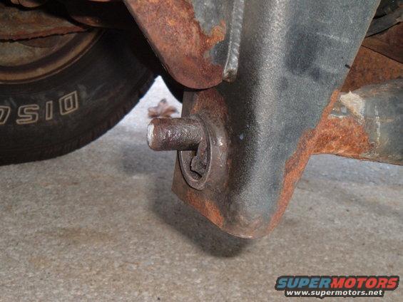 Rusty suspension part with a pin extending from a bracket, near a tire