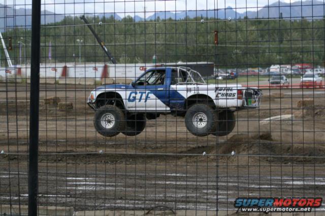Pickup truck with "GTF" and "TOTAL CHAOS" graphics airborne over dirt track