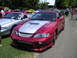 2009 Ford Mustang - A customized red convertible is parked on grass next to a silver convertible, with people milling around in the background.