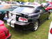 2009 Ford Mustang - Black Ford Mustang with silver racing stripes parked on grass with other cars.