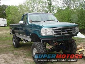 Green pickup truck with large tires and lifted suspension. Some boxes are on the ground nearby