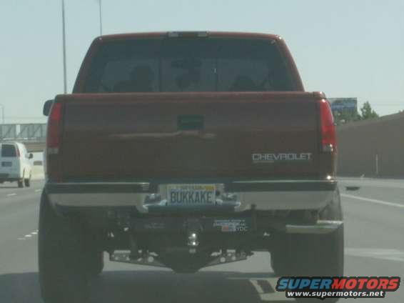Rear view of a red Chevrolet pickup truck on the highway. Another white van is visible in the left lane