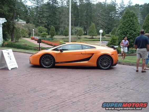 orange sports car parked on brick driveway, people standing nearby