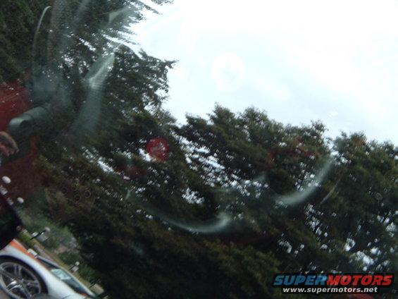Silver car side view, partially obscured by windshield glare and trees
