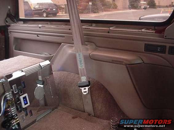 Interior shot of a 1990s SUV, showing the passenger side door panel, seatbelt, and a digital display. Another SUV is visible through the window