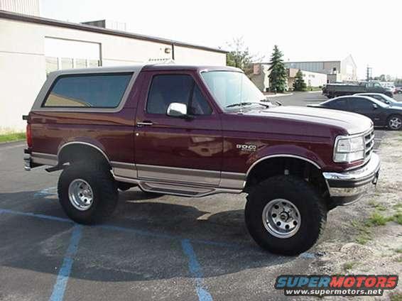 Maroon Ford Bronco parked in a lot, showing its side and front quarter panel. It has a grey top and large tires