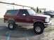 1996 Ford Bronco - This maroon Ford Bronco is parked in a lot, showing off its lifted suspension and aftermarket wheels.