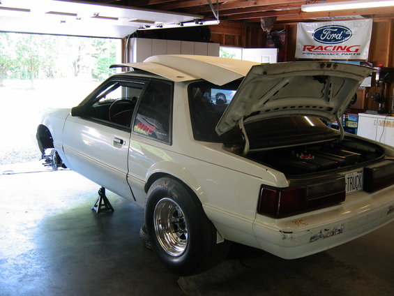 white 1992 Ford Mustang on jack stands in a garage, hood open, trunk open