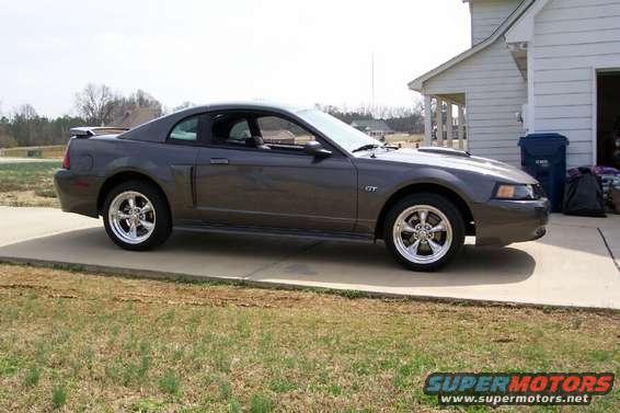 Dark gray Ford Mustang GT parked on a concrete driveway next to a house