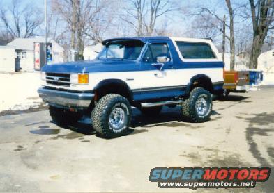 Blue and white Ford Bronco with aftermarket wheels and tires, parked on asphalt